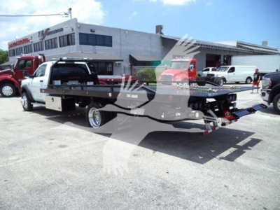 Ram 5500 rollback tow truck in a dealership lot showing flatbed and rear equipment.