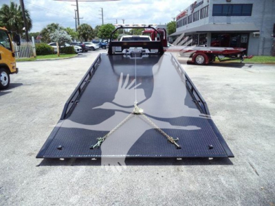 Ram 5500 rollback tow truck with long black steel ramp, chain hooks, and support bars in foreground.