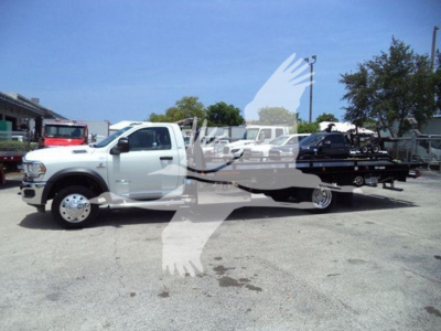 Ram 5500 rollback truck in showroom lot with white cab and black flatbed, side view, no visible text on vehicles.
