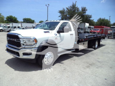 Ram 5500 tow truck with a flatbed in a dealership lot, side view showing white cab and long black flatbed.