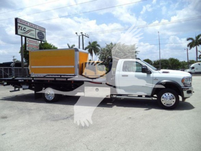 Ram 5500 rollback tow truck with flatbed and orange equipment container on the bed; dealership sign visible in background.