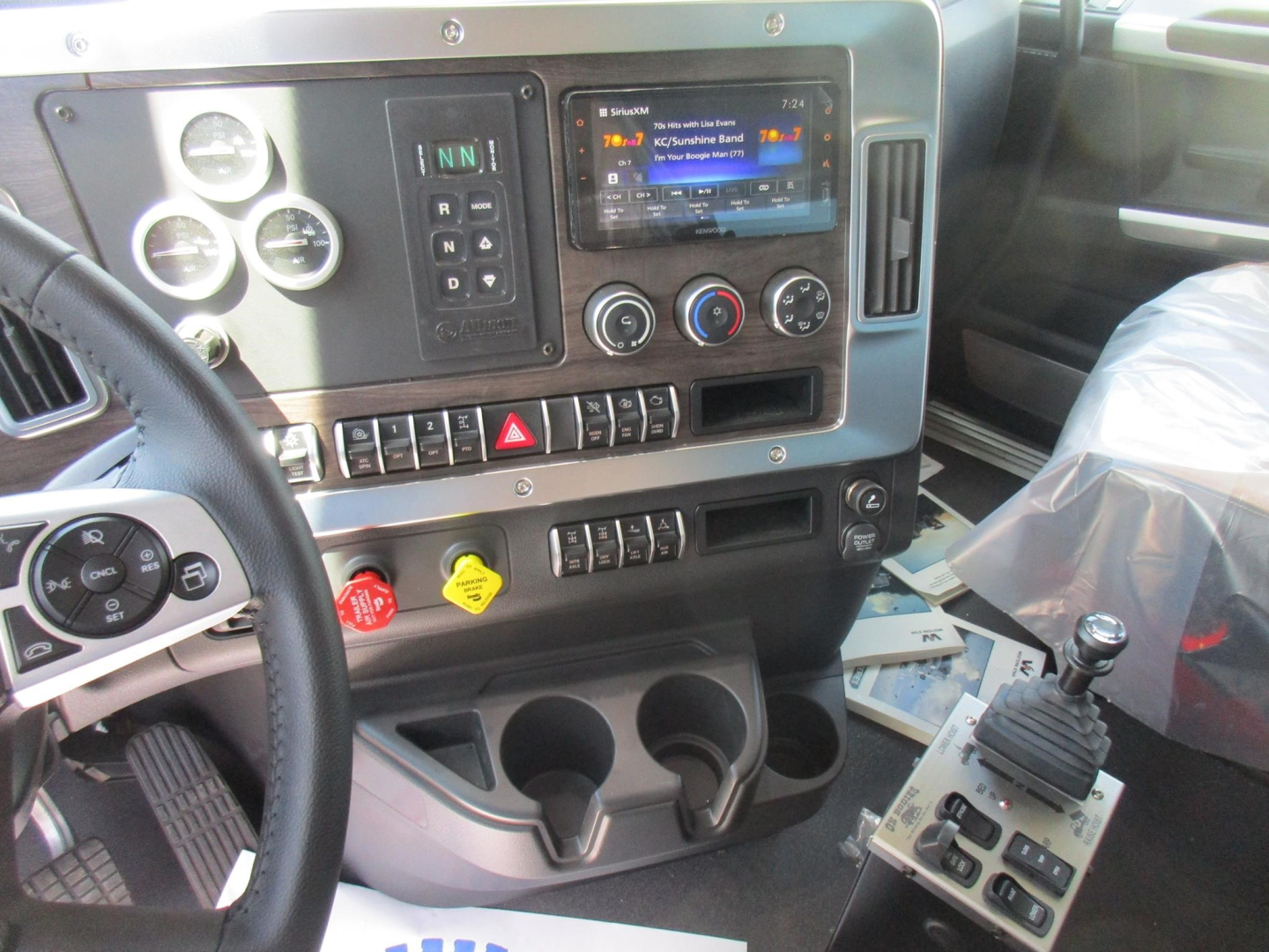 Dashboard of new Western Star 49X dump truck showing instrument cluster, touchscreen infotainment, control knobs, gear selector, cup holders, and multiple switches.