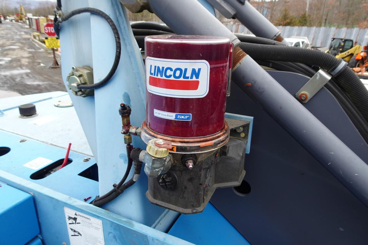 Truck crane-like machine showing Lincoln hydraulic filter/ fluid reservoir with blue frame and hoses.