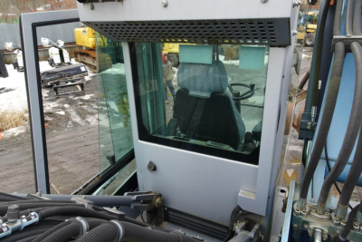 Cab view of a 2012 Terex MHL 331 telescopic handler cabin with glass windows and operator seat, hydraulic lines in foreground, utility yard background.