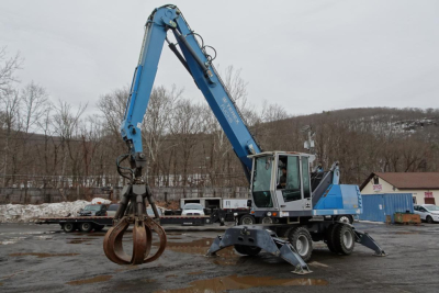Terex MHL 331 knuckle boom crane in service mode with grapple attachment, blue color, mounted on a wheeled chassis, in an outdoor yard.