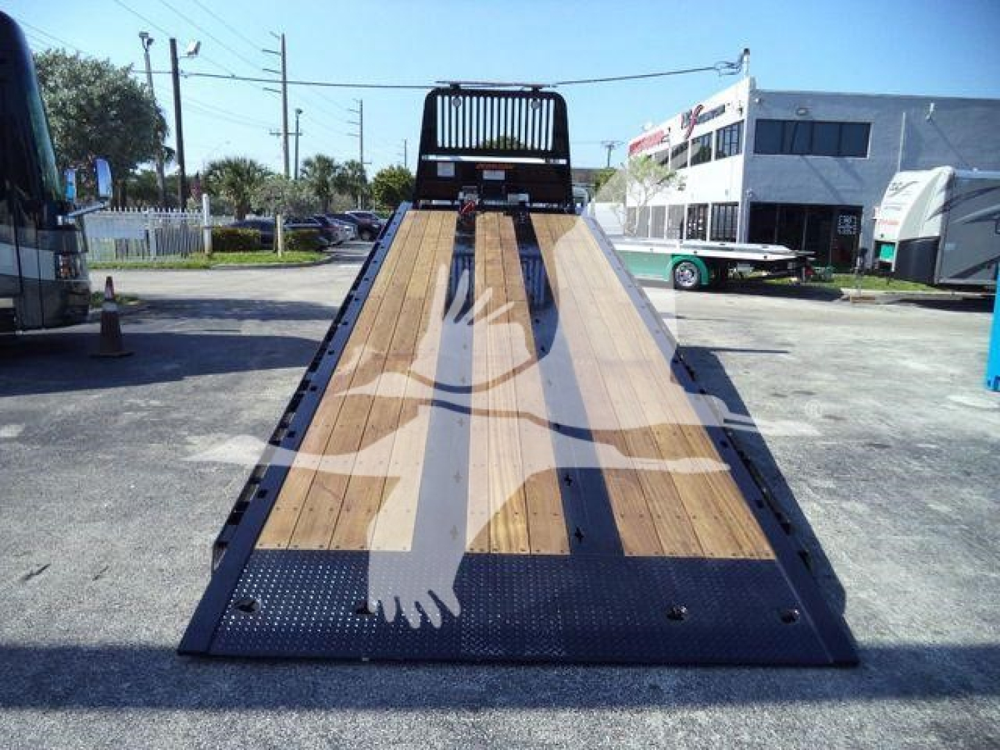 Kenworth T880 rollback flatbed truck in a lot, wooden deck surface with metal frame and ramp, rear view showing loading ramp and wheel wells.