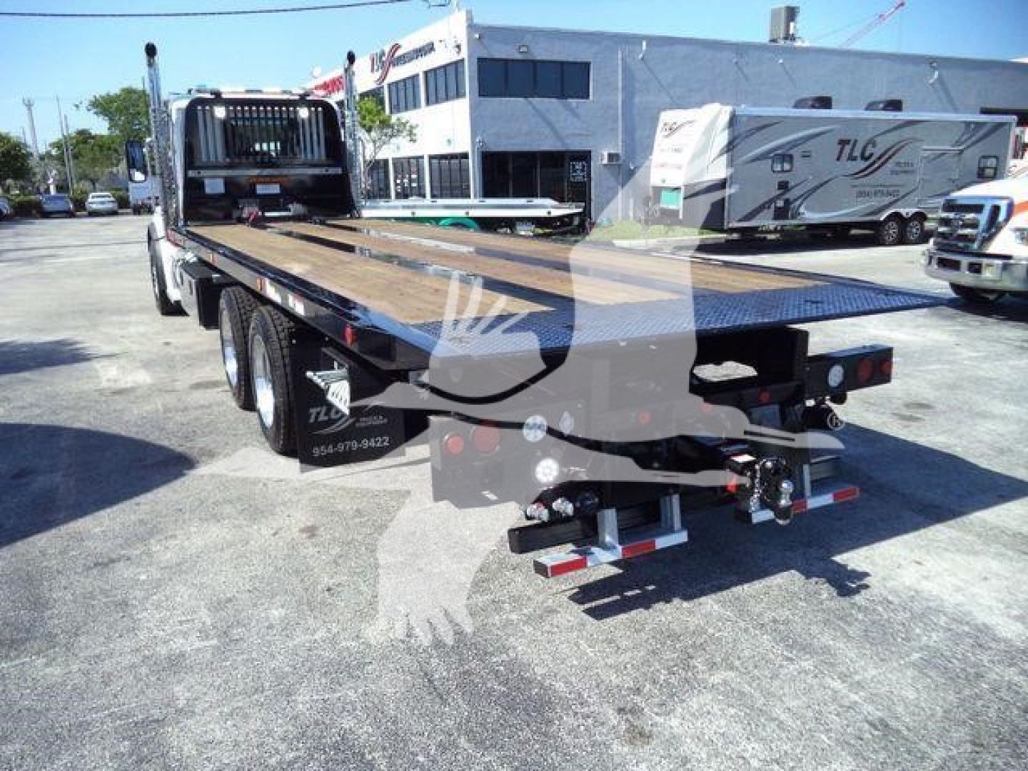Kenworth T880 rollback flatbed truck rear view showing bed with ramps and hitch, with dealership lot in background.