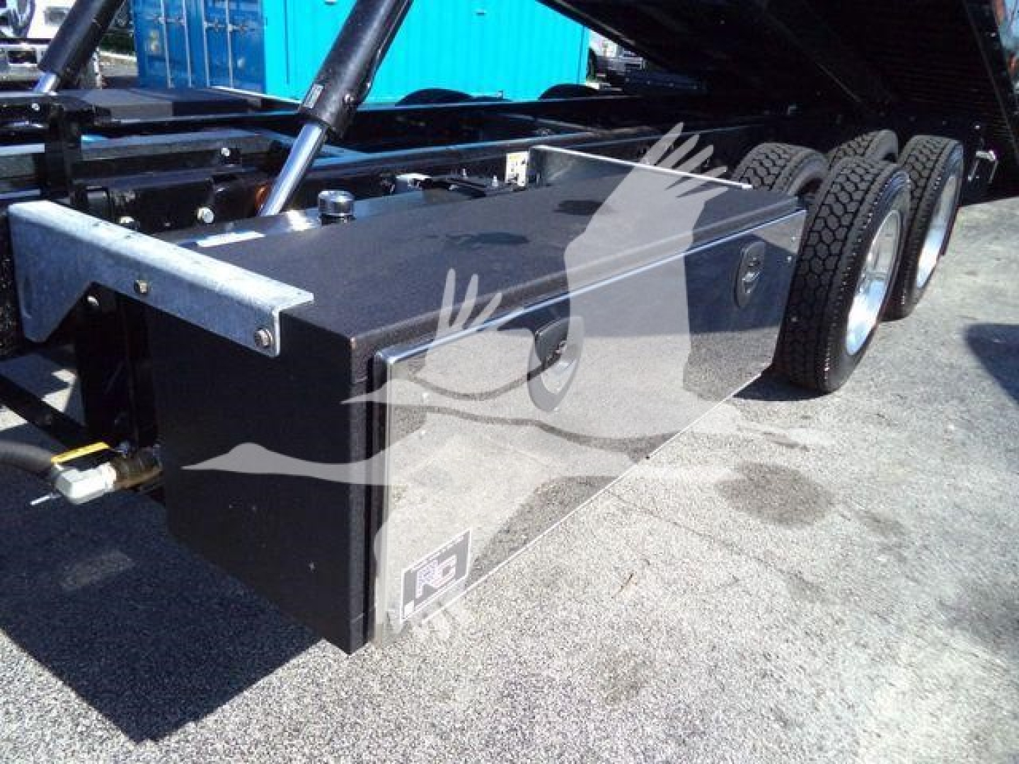 Kenworth T880 rollback truck chassis with a large rectangular tool/storage box and triple rear axles showing undercarriage and hydraulic components.