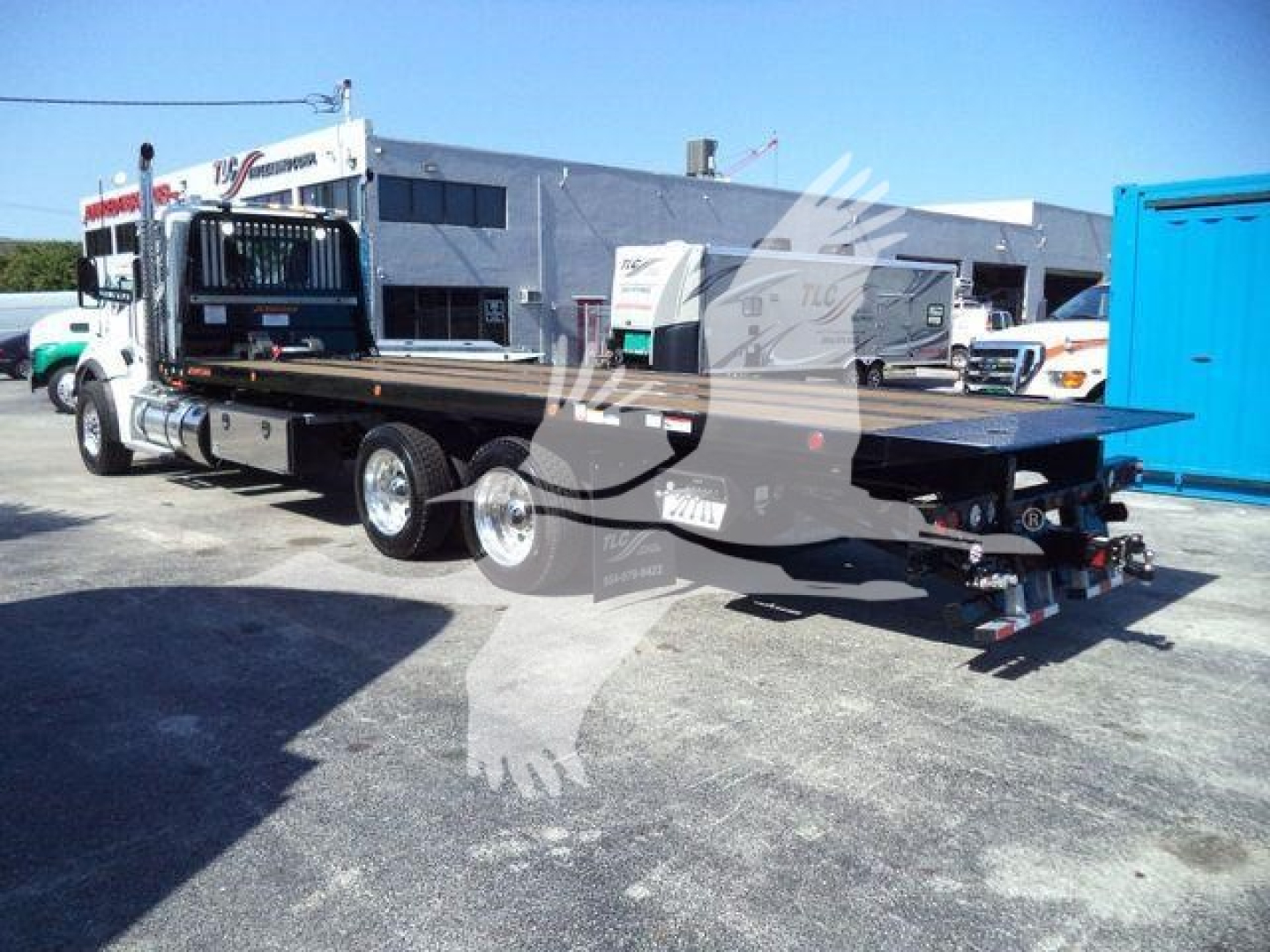 Kenworth T880 rollback truck trailer in a lot, flatbed extended with hydraulic ramps and dual rear axles.