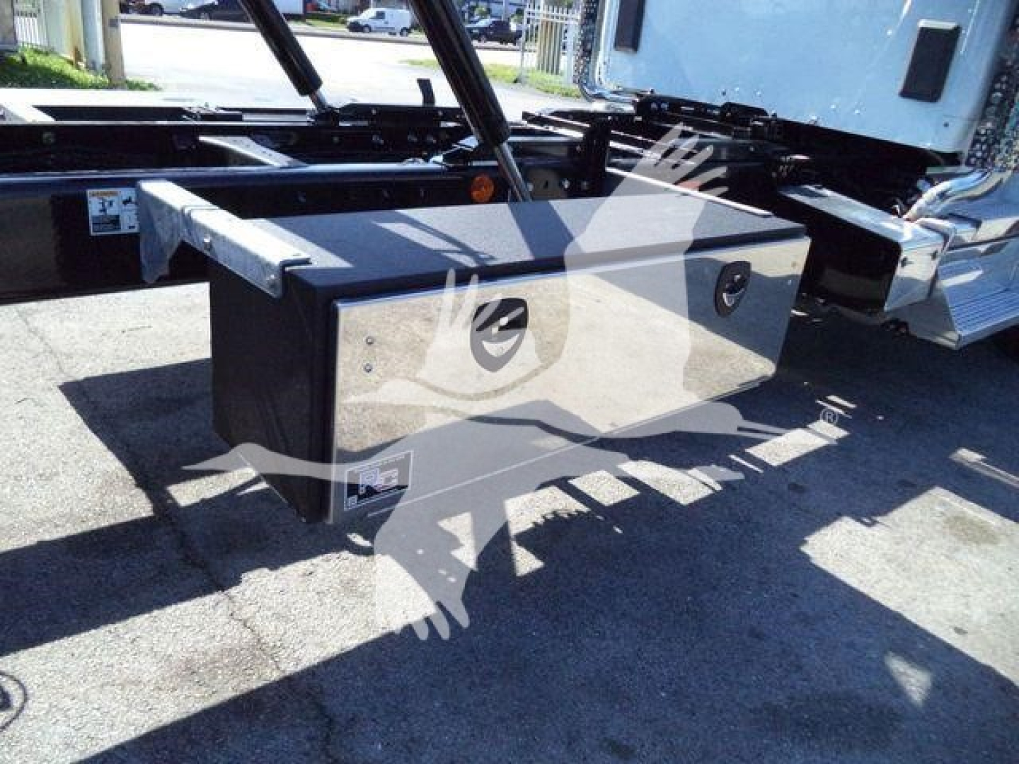 Kenworth T880 rollback truck chassis showing a black storage box mounted under the frame with metal latches and a small orange reflector.