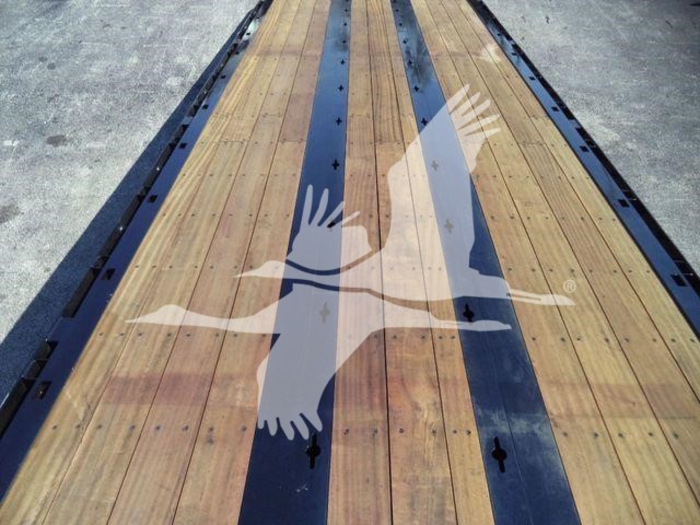 Trailer deck with wooden planks and black side rails, showing a white silhouette of a hawk with wings spread.