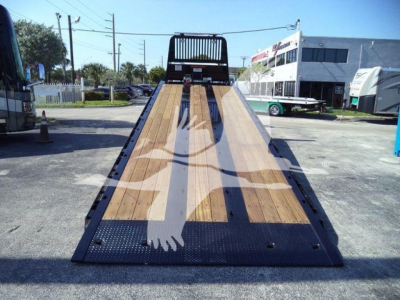 Kenworth T880 rollback flatbed truck in a lot, wooden deck surface with metal frame and ramp, rear view showing loading ramp and wheel wells.