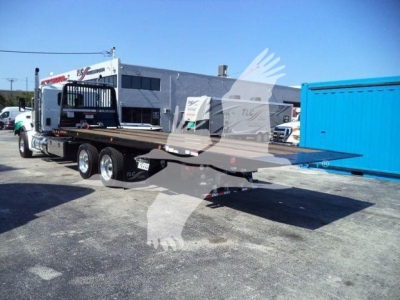 Kenworth T880 rollback truck trailer showing flatbed with dual rear axles and metal deck; background shows building and blue container.