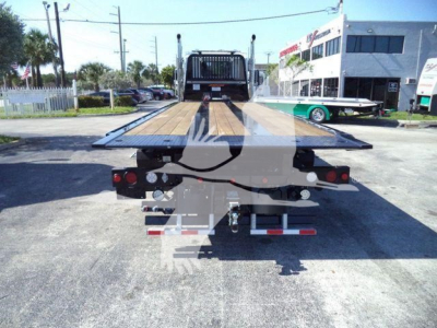Tow truck flatbed body seen from rear with loading ramps extended, Kenworth T880 in background, dealership lot, stock number J68214.