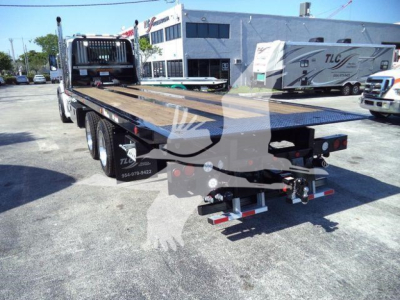 Kenworth T880 rollback flatbed truck rear view showing bed with ramps and hitch, with dealership lot in background.