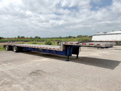 Trailer showing a long blue drop deck semi-trailer with wheels on left side and extended landing gear.