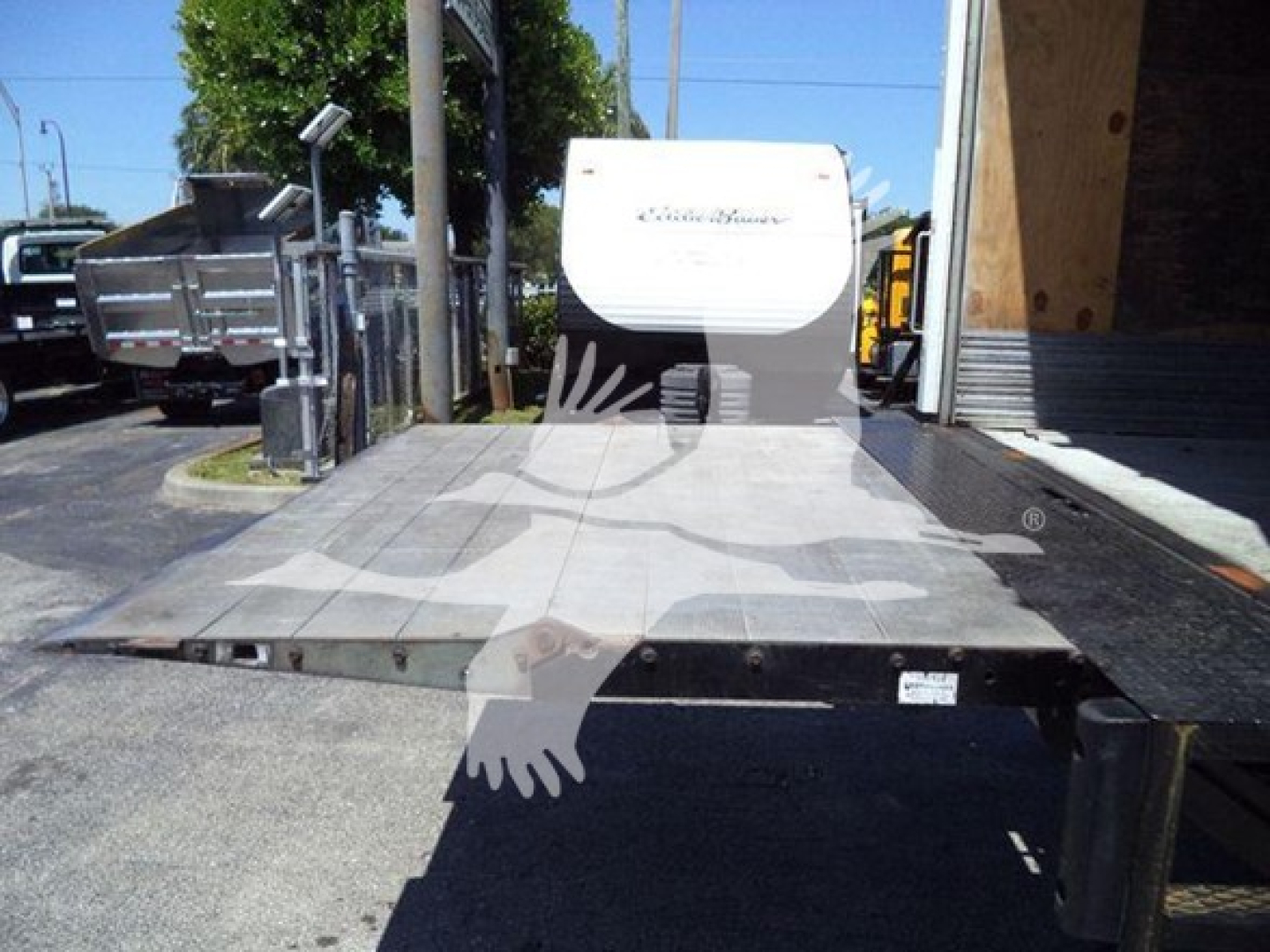 Freightliner M2 106 transfer bed area with flatbed platform and hydraulic ramp in front, truck chassis visible in background.