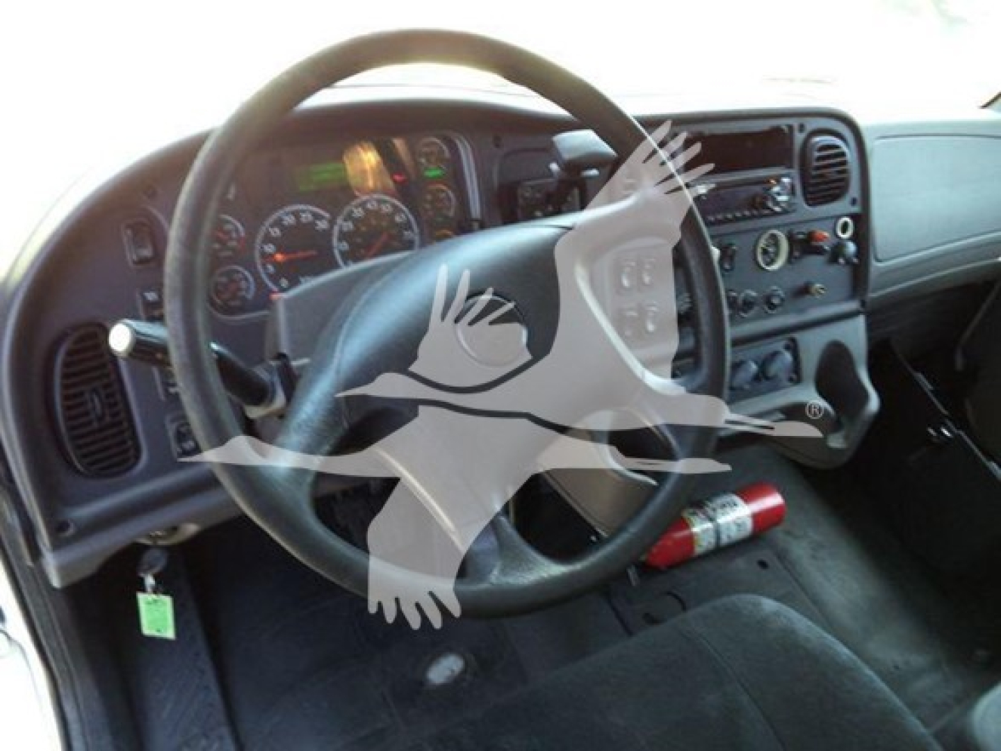 Truck interior showing steering wheel, dashboard with gauges, center console, and a fire extinguisher mounted under the dash.