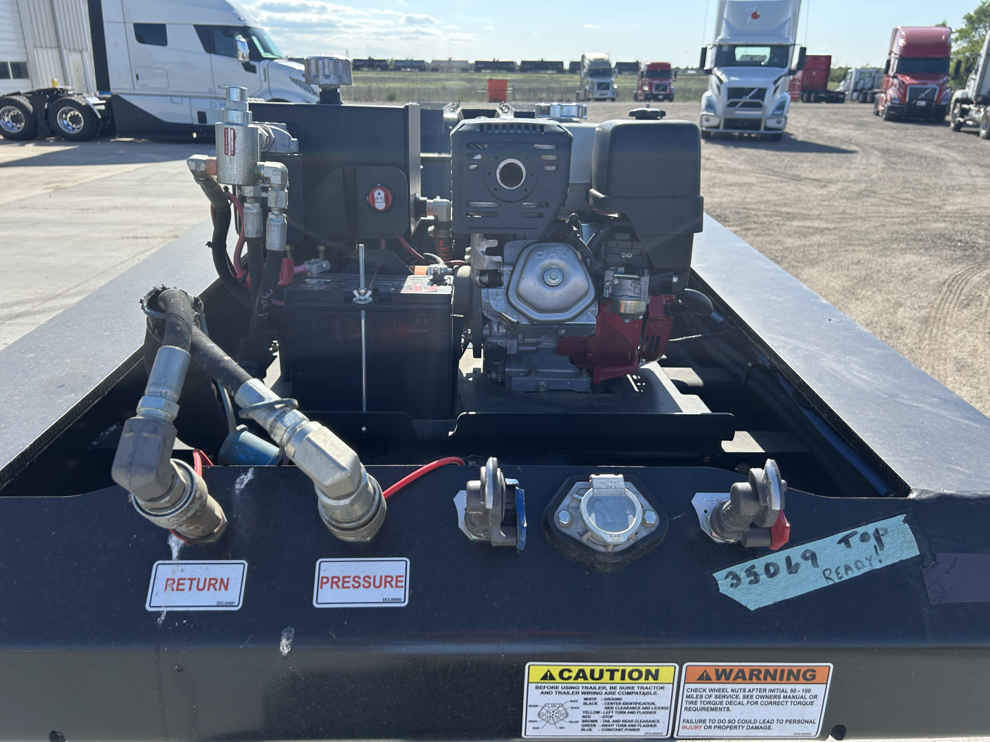 Trailer deck showing a Load King 503/554 SF lowboy with engine and hydraulic components, labels reading RETURN and PRESSURE, warning sticker, and a CAUTION/WARNING plate visible