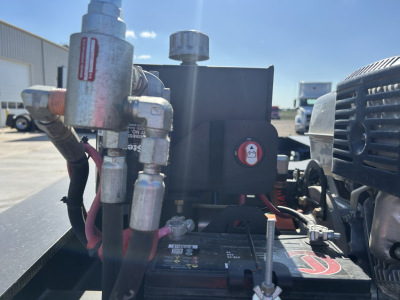 Trailer engine bay area showing hydraulic lines, fittings, and control panel with battery and engine components.