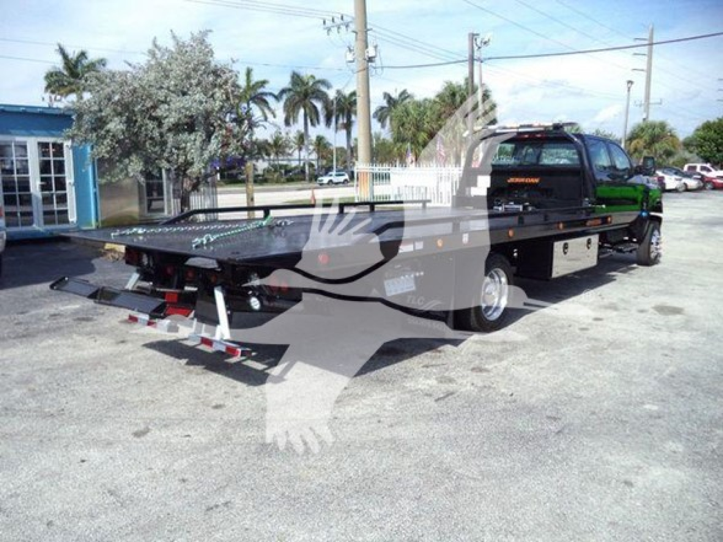Roll-back tow truck in a parking lot showing flatbed bed and hydraulic equipment with branding on door.