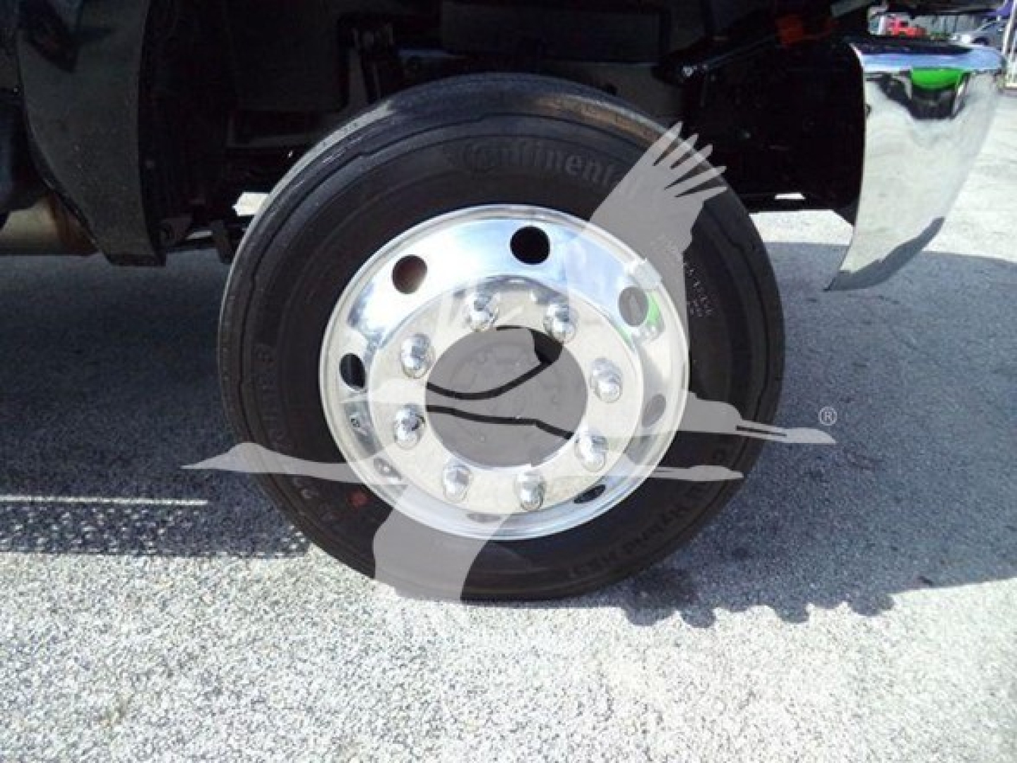 Truck front wheel and tire close-up showing steel rim with bolted hub and green valve cap, part of International CV rollback truck.