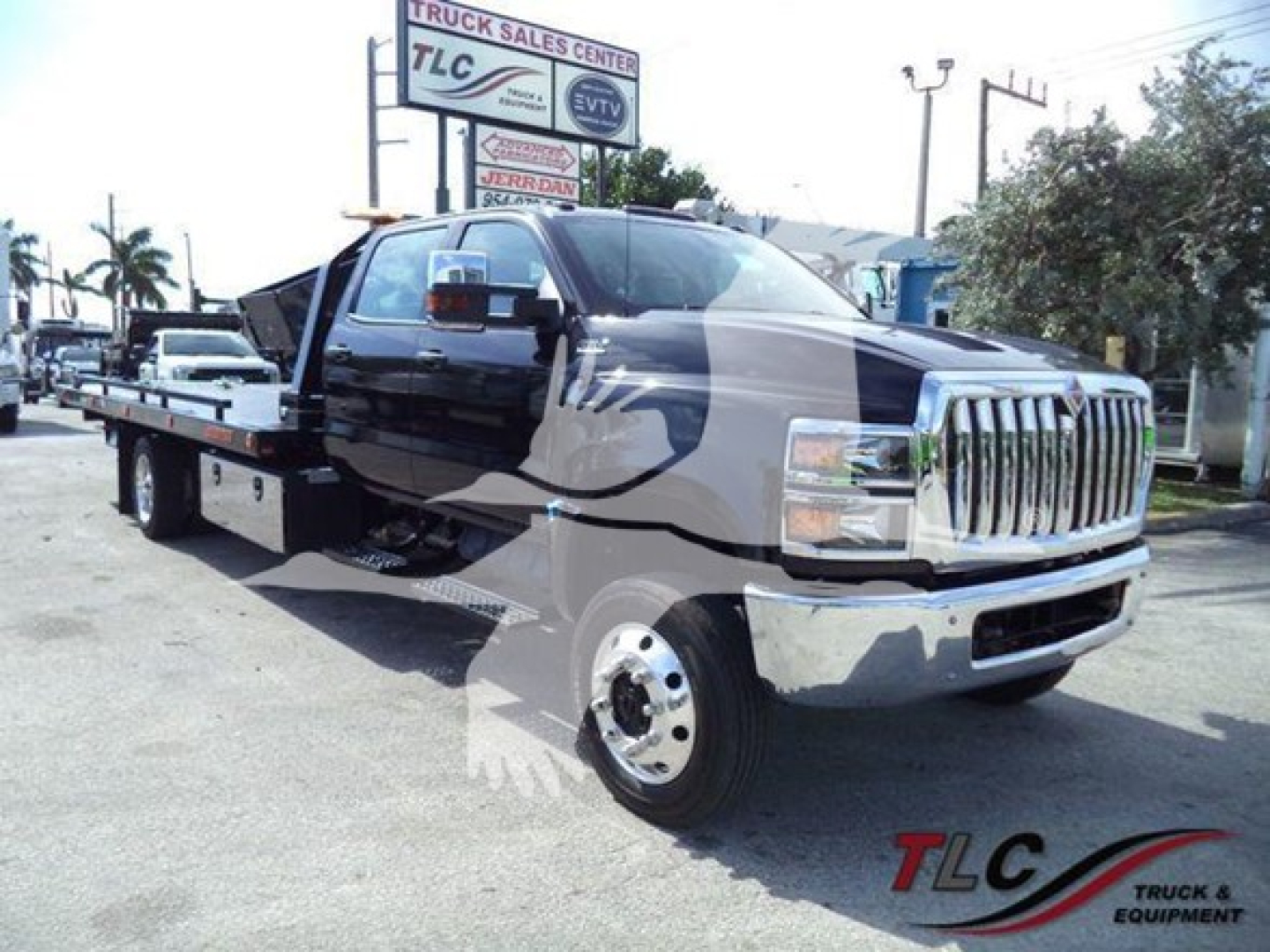 Truck/flatbed tow truck with extended cab showing chrome grille and dual rear wheels.