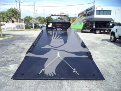 Flatbed tow truck bed on a 2023 International CV with a crossed chain setup and rear cab visible in background.