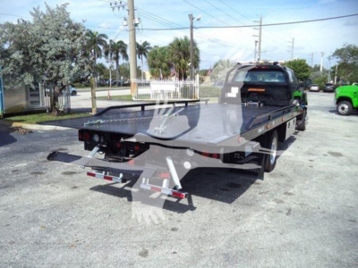 Flatbed tow truck in a parking lot with rear view, showing long aluminum bed and rear lighting.