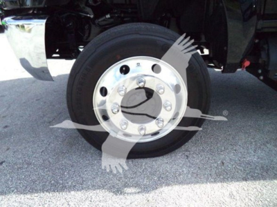 Truck wheel with shiny chrome hubcap and black tire, undercarriage visible, front left wheel of a 2023 International CV rollback truck.