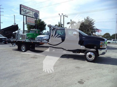 Truck showing a flatbed rollback tow truck with a two-tone cab and large extended flatbed in a dealership lot.