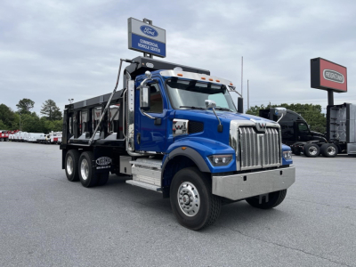 Blue Western Star 47X dump truck in a dealership lot, heavy-duty chassis, chrome front bumper, dual rear axles, dump bed.