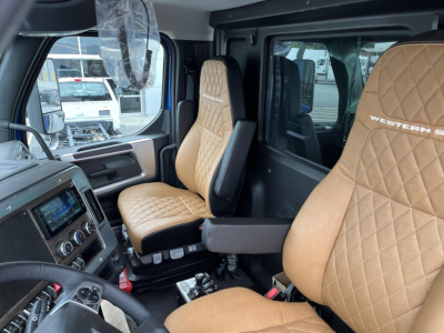 Interior of a new Western Star 47X truck cockpit with tan quilted seats, visible driver and passenger seats, dashboard controls, and steering wheel.