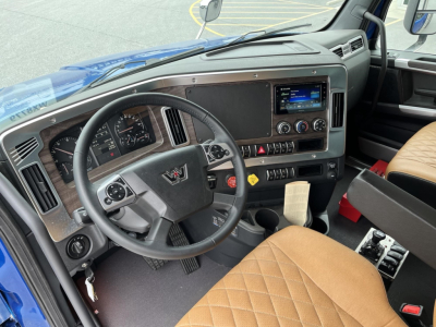 Interior view of a new Western Star 47X dump truck cab showing steering wheel, dashboard, touchscreen infotainment, and tan diamond-stitched seats.