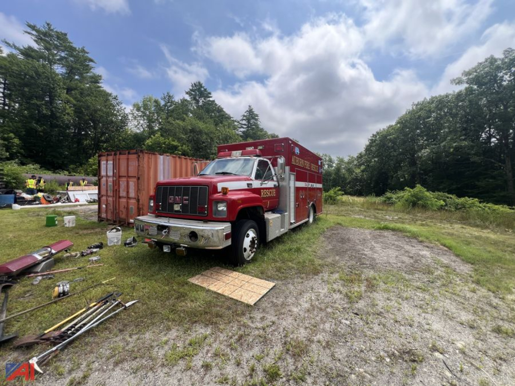GMC C7500 fire truck in an outdoor lot with tools around, red body with emergency markings.