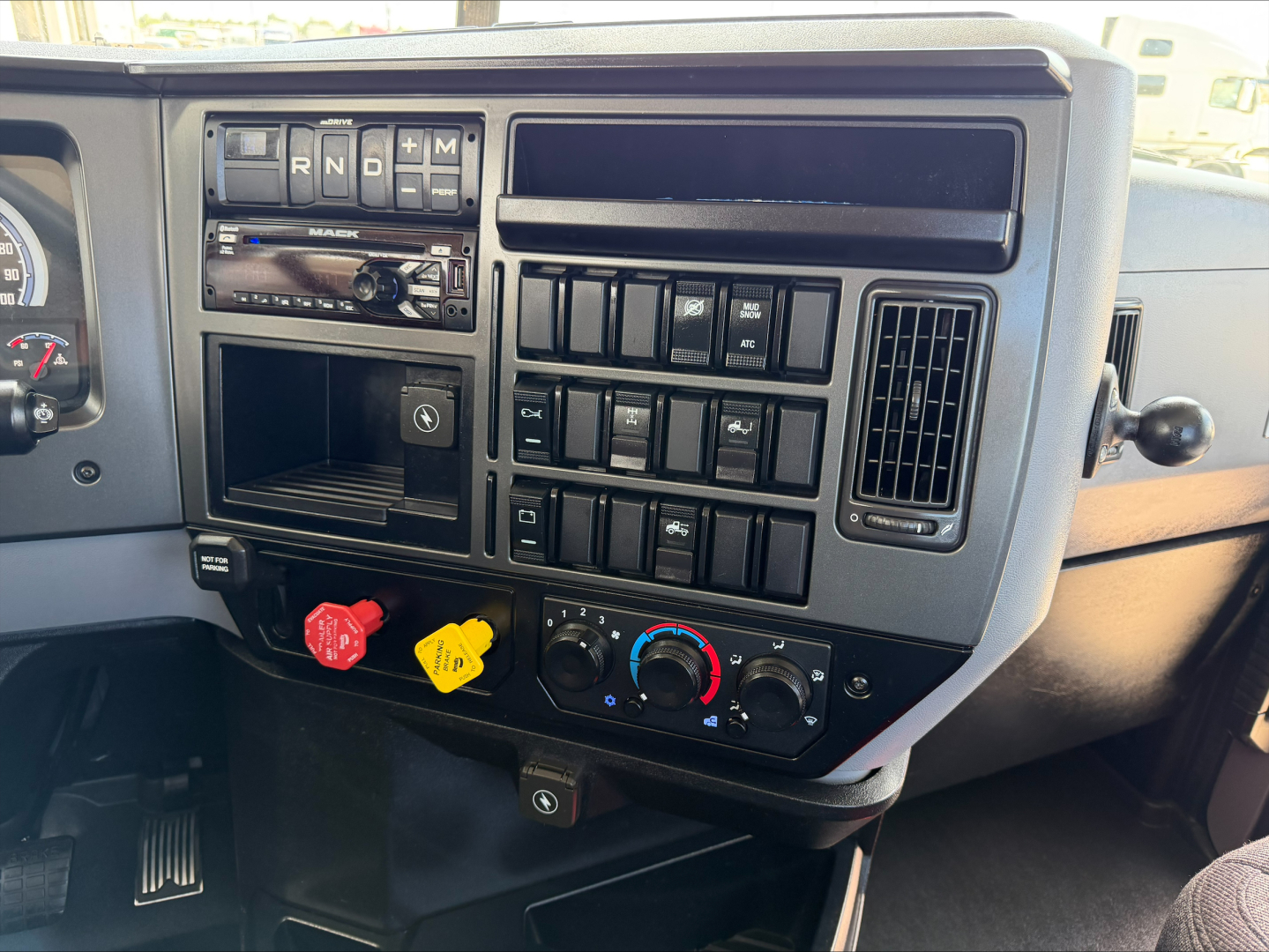 Dashboard of a 2020 Mack Anthem tractor showing climate controls, radio, switches, and red and yellow knob icons. Visible text includes R N D M on the gear selector area and various switch labels.
