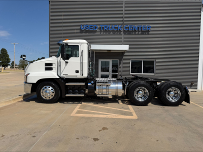 Truck in front of Used Truck Center building: 2020 Mack Anthem conventional daycab side view with white cab, dual rear axles, chrome fuel tanks, and stock number W0009.