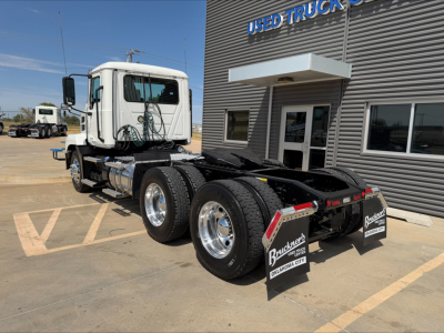 Truck rear/side view of a white Mack Anthem daycab tractor with dual rear axles and chrome fuel tanks, parked outside a used trucks dealership.