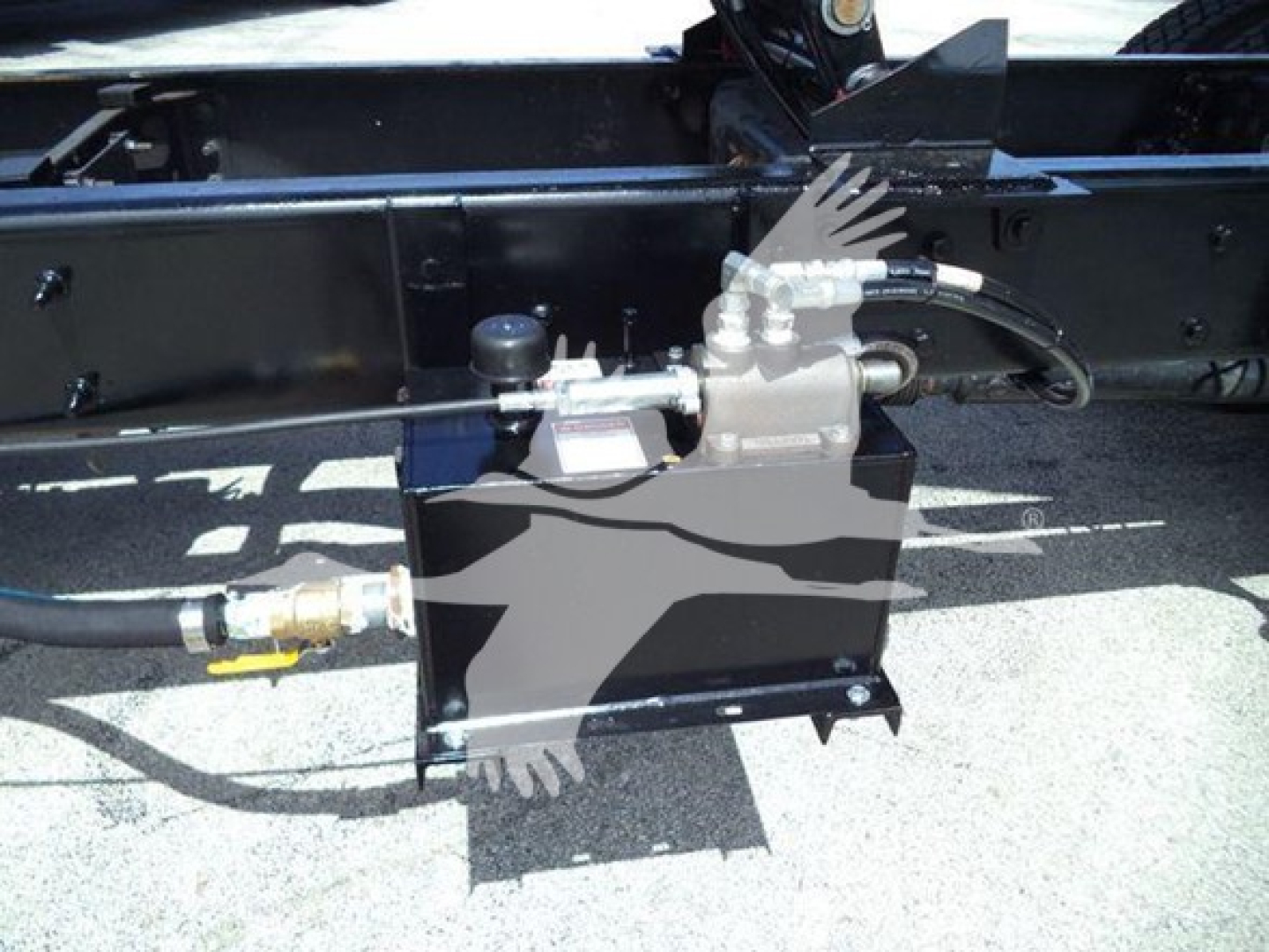 Dump truck undercarriage with hydraulic pump assembly and hoses mounted on black metal frame.