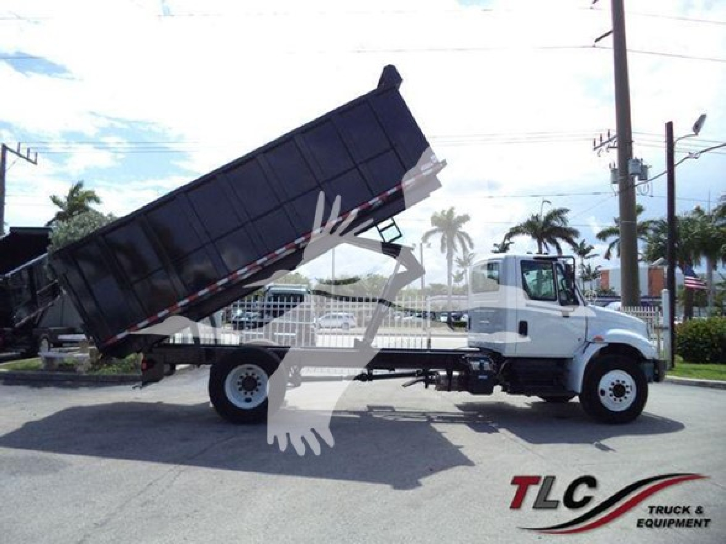Dump truck with raised dump bed in transport yard, International Durastar 4300 model, white cab, black dump body, side view showing lifting mechanism and rear wheels.