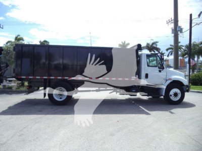 Truck side view showing dump bed with black container and white cab, with red/white side reflector tape along the lower body.