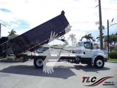Dump truck with raised dump bed in transport yard, International Durastar 4300 model, white cab, black dump body, side view showing lifting mechanism and rear wheels.