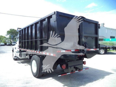 Dump truck rear and side view showing dump bed with vertical ribs, rear taillights, and bumper. Visible text on tail area includes model and branding not clearly legible.