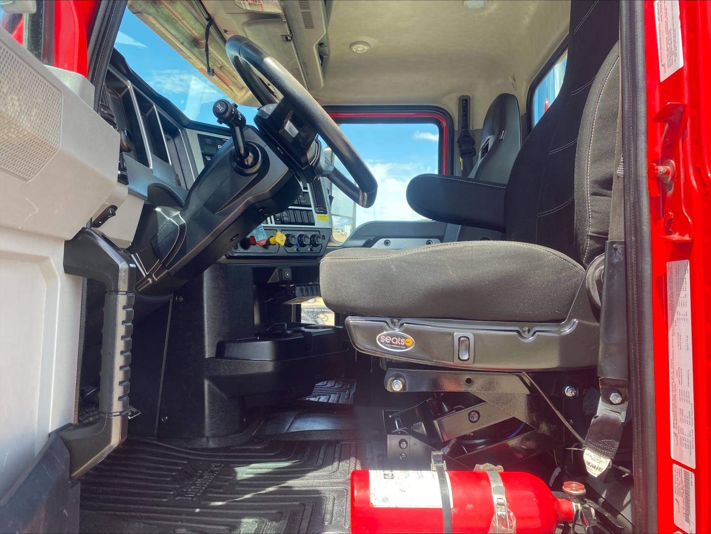 Cab interior of 2021 Mack Anthem daycab showing steering wheel, dashboard controls, driver's seat, and red exterior door frame.