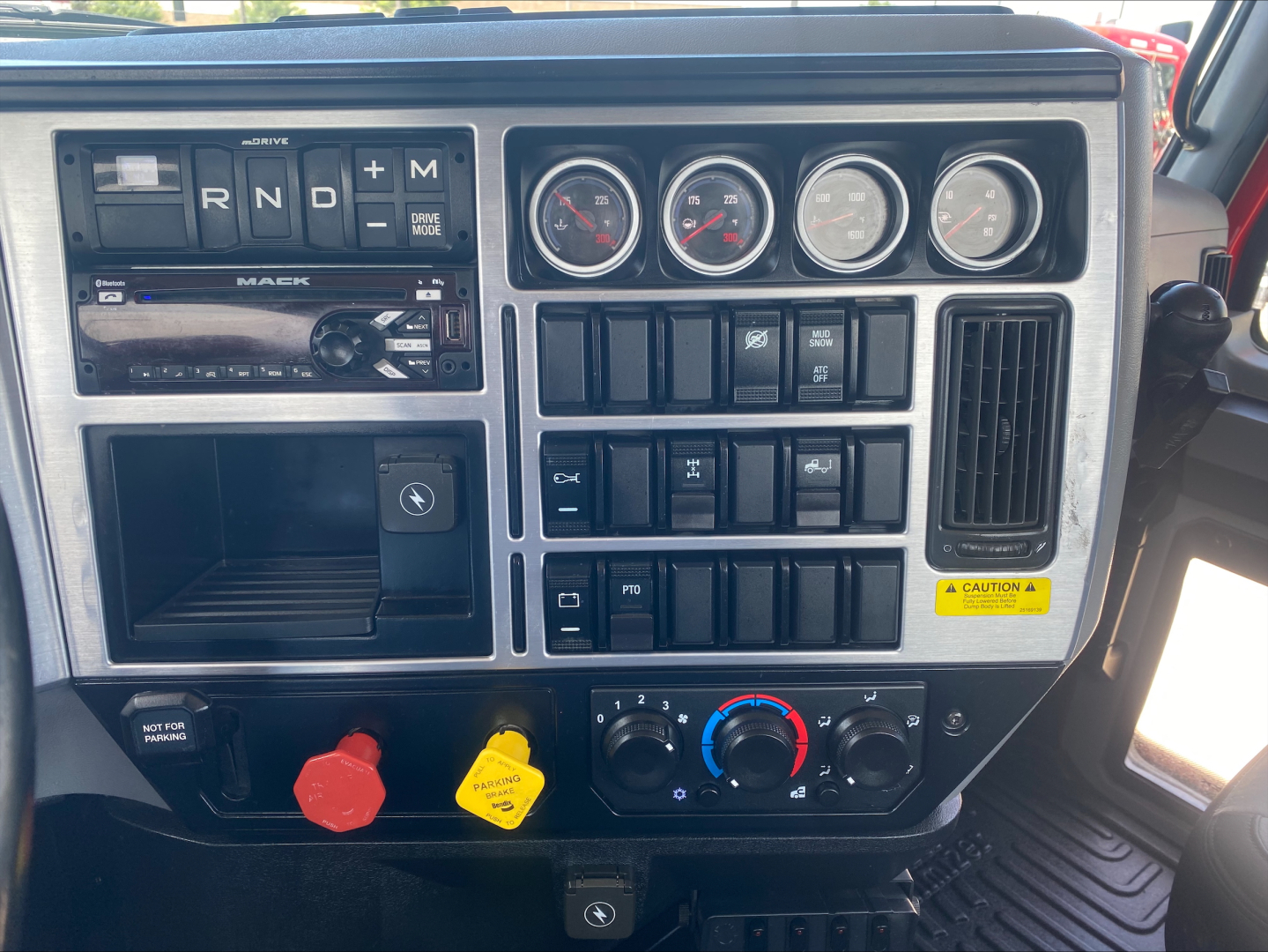 Dashboard view of a 2021 Mack Anthem truck showing R,N,D, and M gear selector, four gauge cluster, control switches, and climate controls.