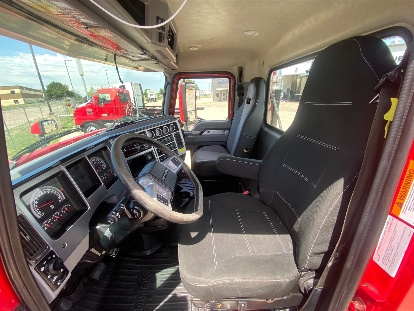 Cab interior of a 2021 Mack Anthem showing steering wheel, dash gauges, driver seat, and door with warning label.