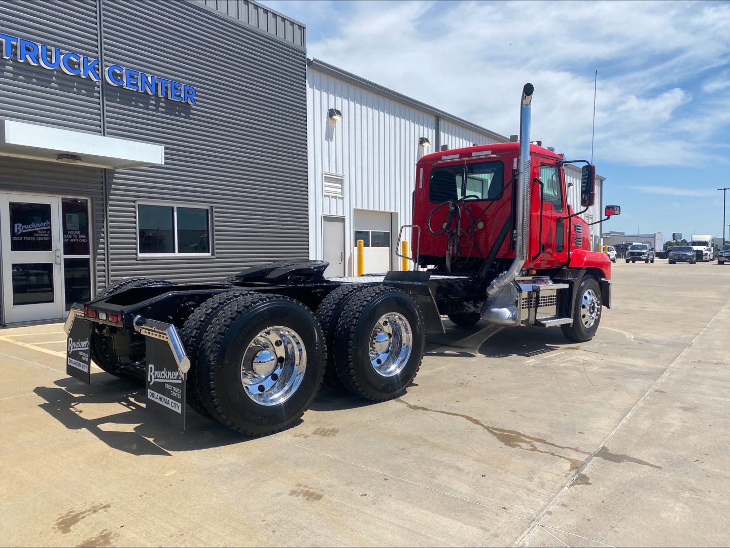 Mack ANTHEM tractor in red cab viewed from rear-left side, dual rear axles, parked outside a truck center building.
