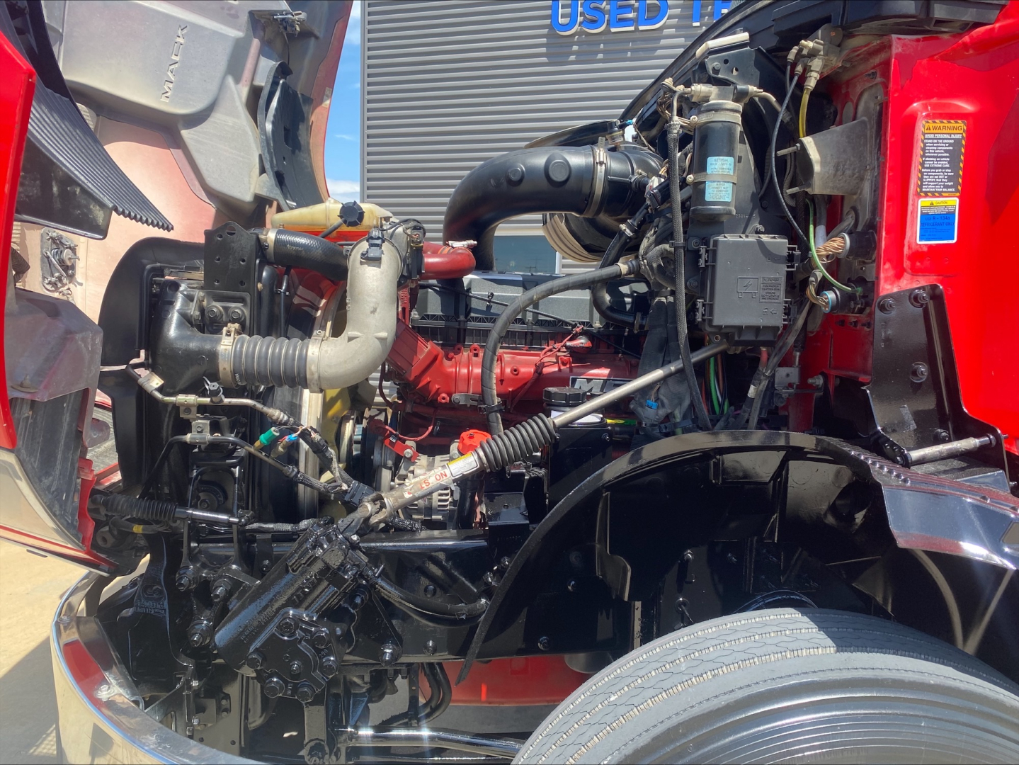 Engine bay of a 2021 Mack Anthem conventional daycab showing engine components, hoses, and wiring in the open hood area.
