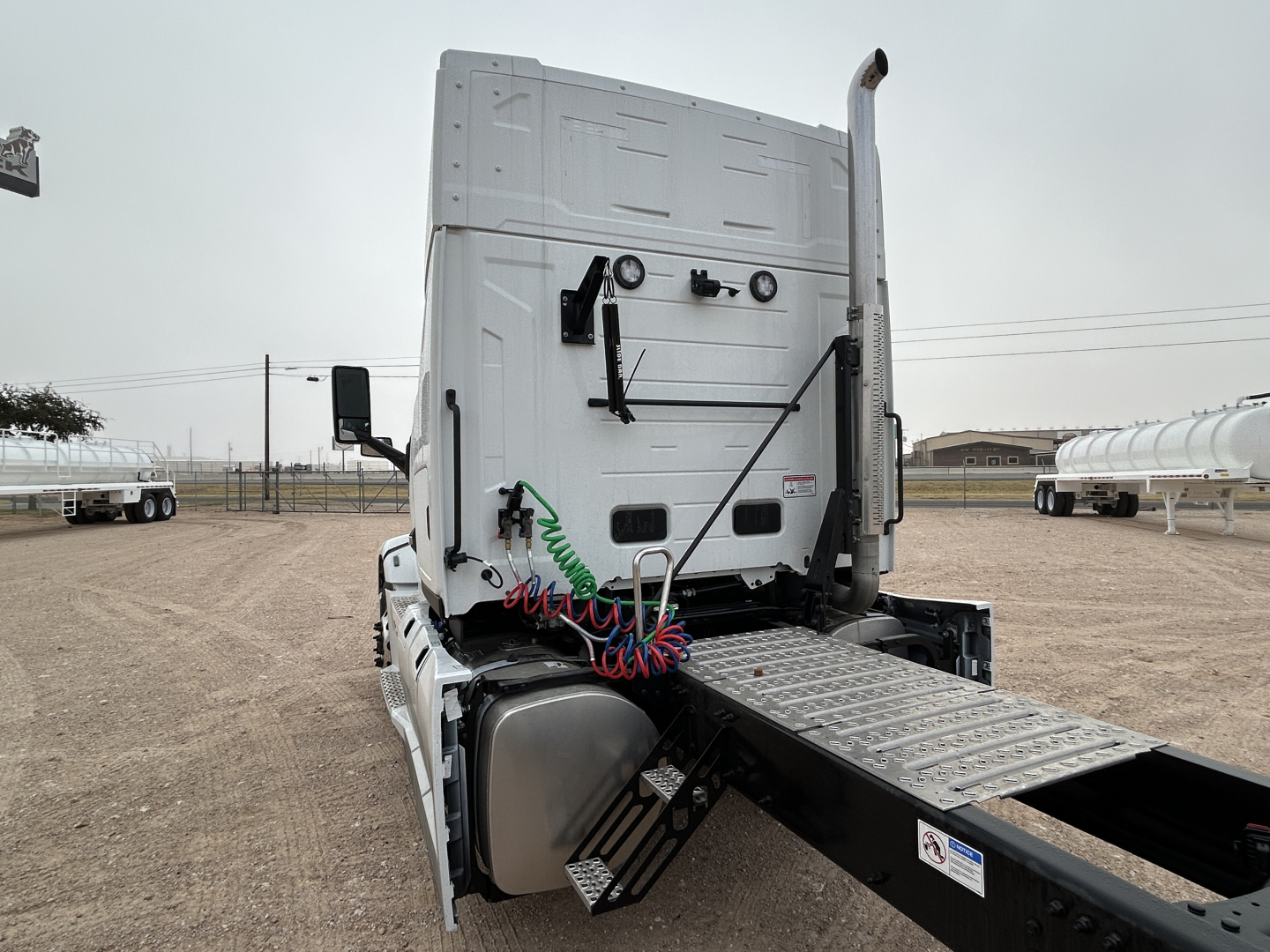 Rear view of a new 2026 Mack PR64T44 truck cab with side-drawn springs, air lines coiled in red/blue, and a metal deck plate for the fifth wheel.