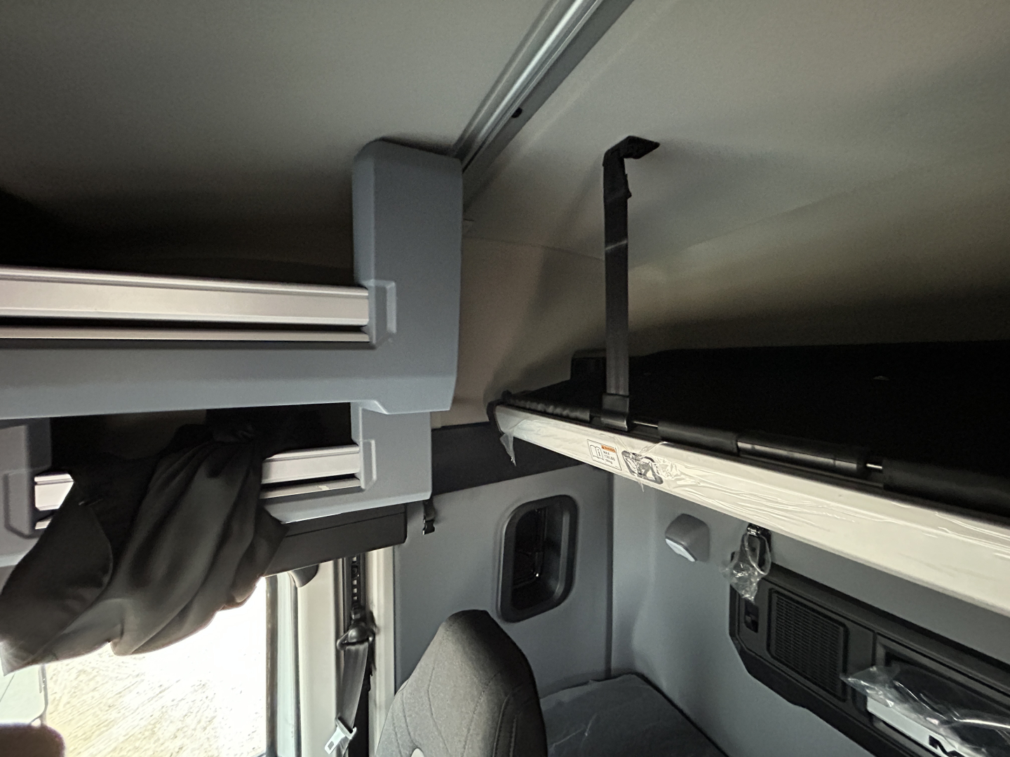 Cab interior of a 2026 Mack PR64T44 sleeper truck showing overhead storage shelf and window area with label stenciling.